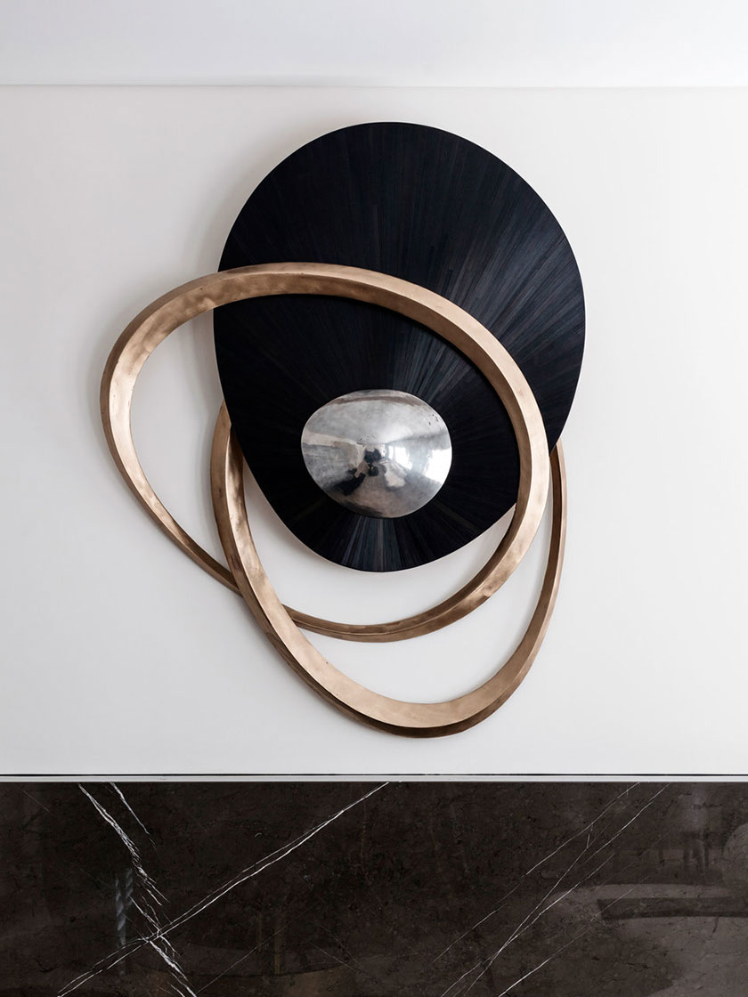 Modern wall sculpture with overlapping circular elements in black and bronze tones.