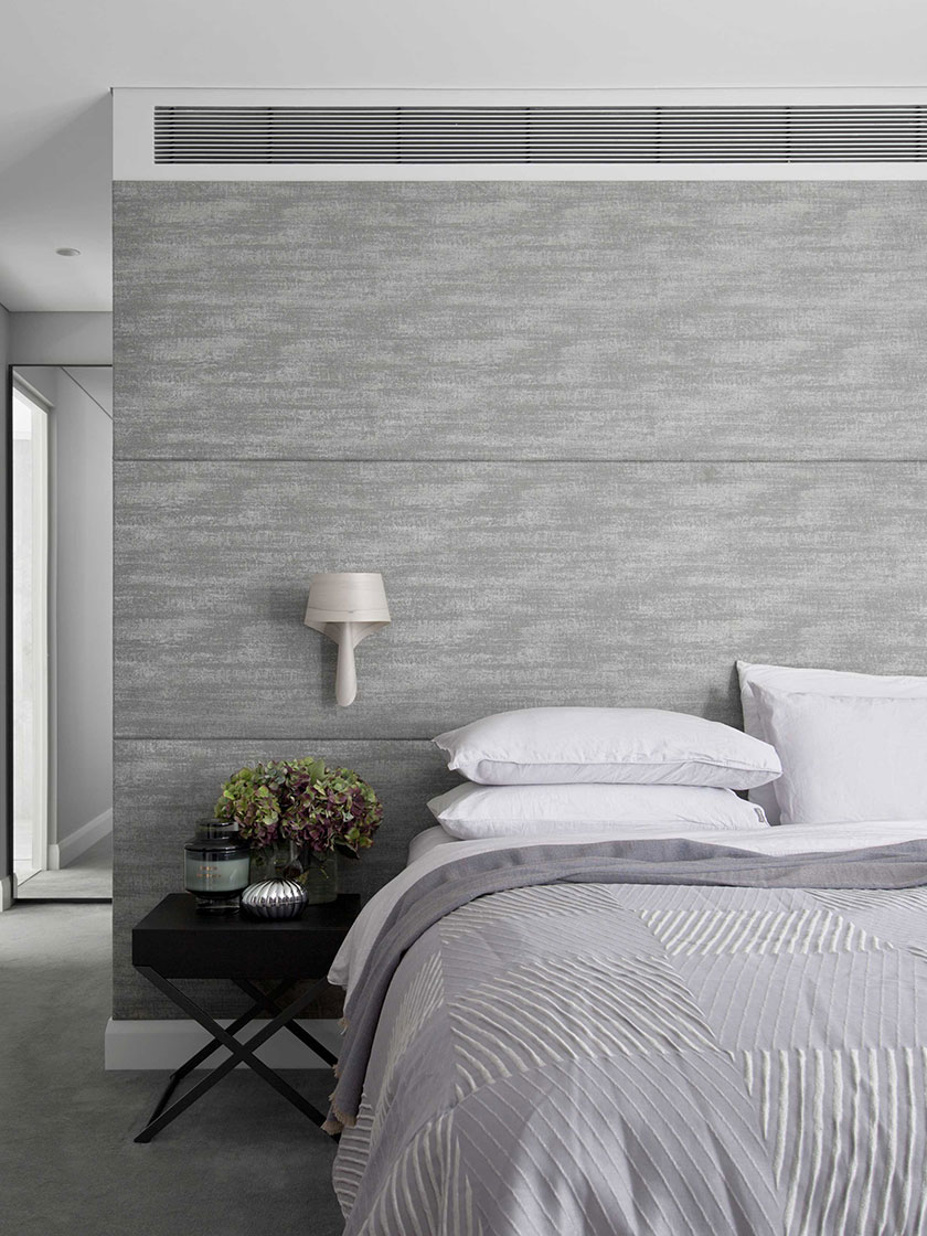 Modern bedroom with grey textured walls, white bedding, and a black nightstand, designed by Nina Maya Interiors